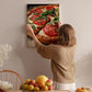 A woman hangs a framed picture of a pizza on a wall in a cozy kitchen setting.