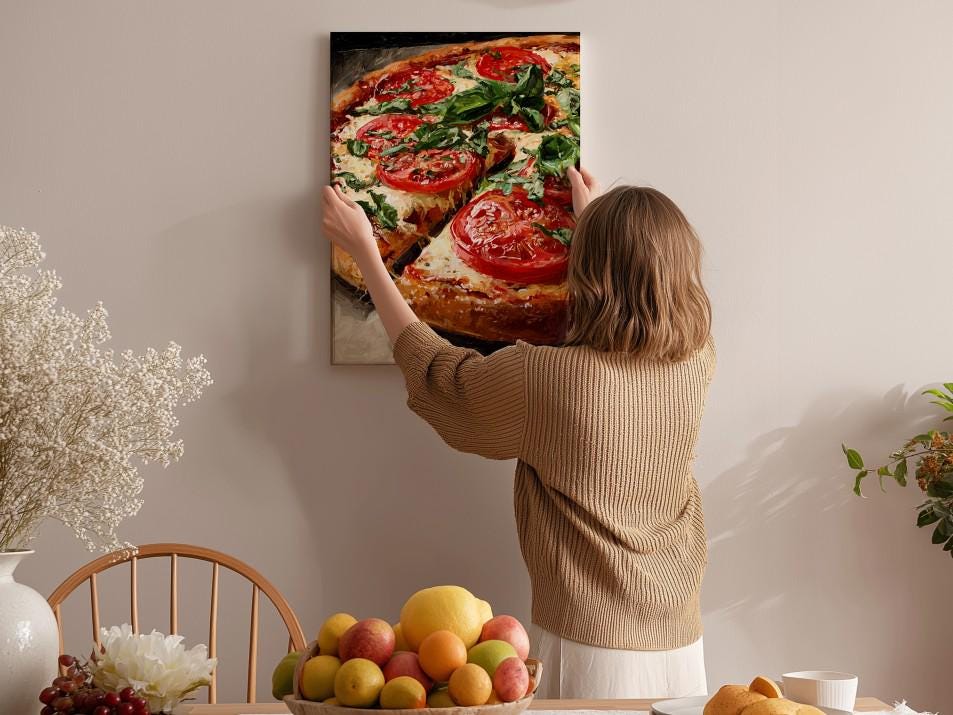 A woman hangs a framed picture of a pizza on a wall in a cozy kitchen setting.