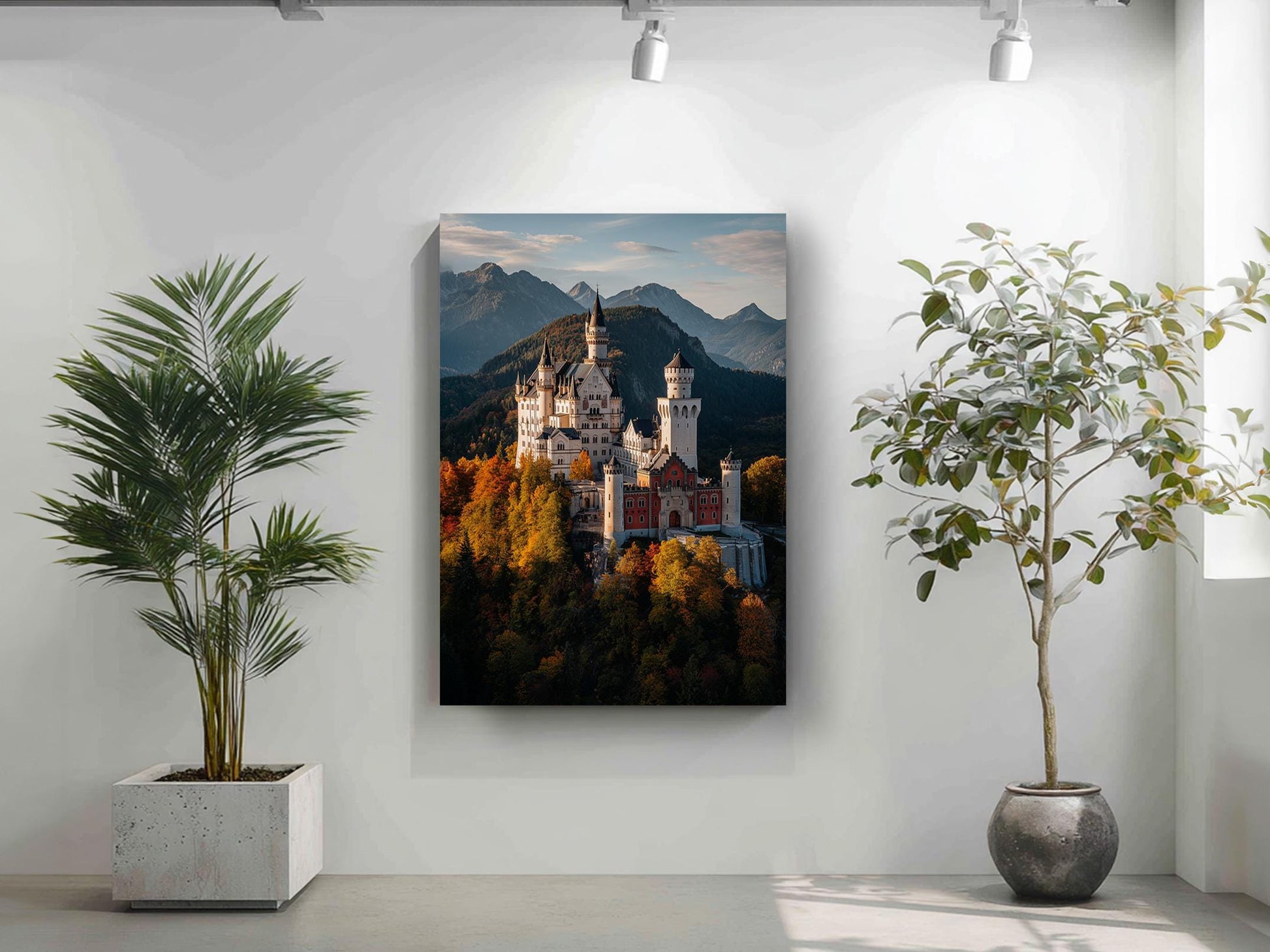 a large painting of a castle on a mountain, with a backdrop of trees and mountains. The painting is hung on a white wall, and there are two potted plants in the foreground, one on the left and one on the right.