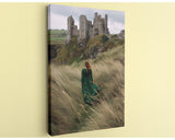 A woman in a green dress walks through tall grass towards a castle in the distance.