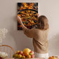 A woman hangs a framed picture of a seafood paella on a wall in a cozy kitchen setting.