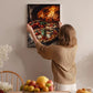 A woman hangs a framed picture of a pizza oven on a wall in a cozy kitchen setting.