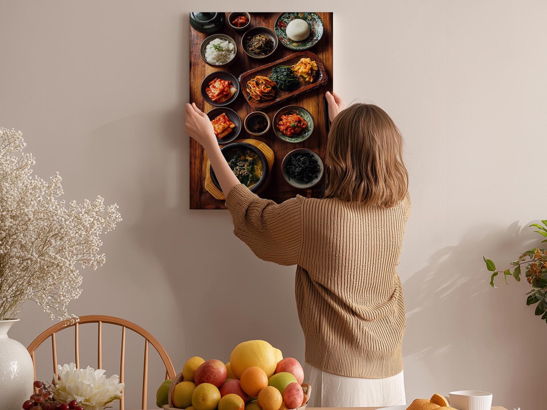 A woman hangs a framed picture of various bowls of food on a wall in a cozy kitchen setting.