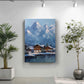 a painting of a snowy mountain village with a lake in the foreground, surrounded by lush greenery. The painting is hung on a white wall, with two potted plants placed on either side of it.