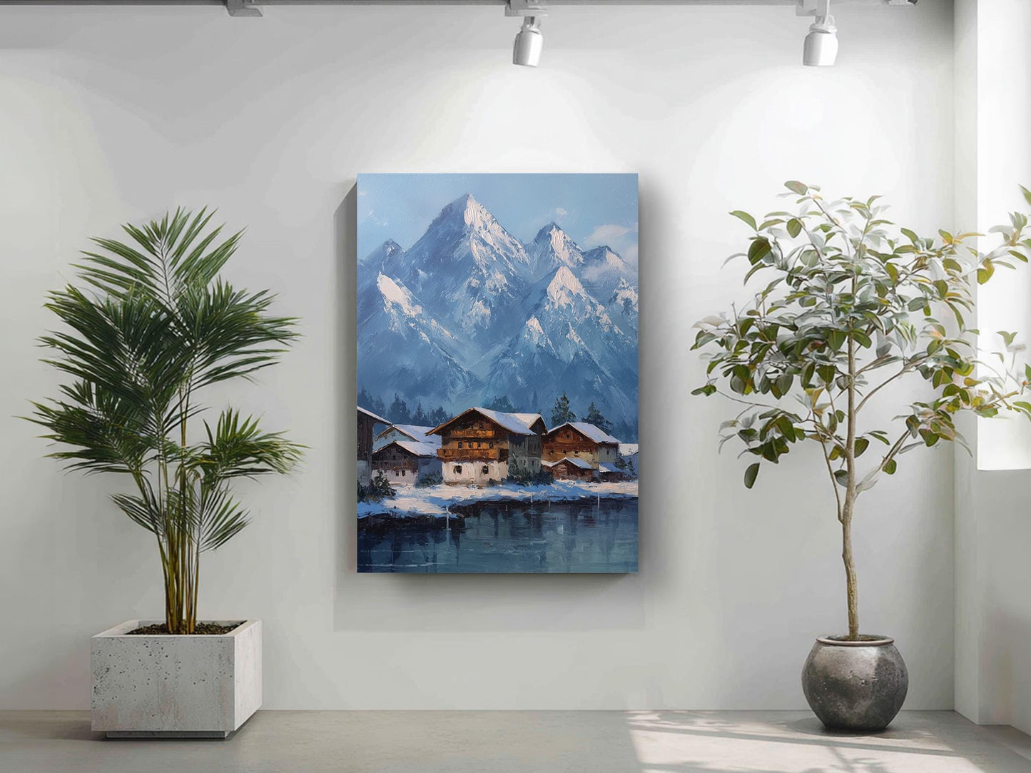 a painting of a snowy mountain village with a lake in the foreground, surrounded by lush greenery. The painting is hung on a white wall, with two potted plants placed on either side of it.