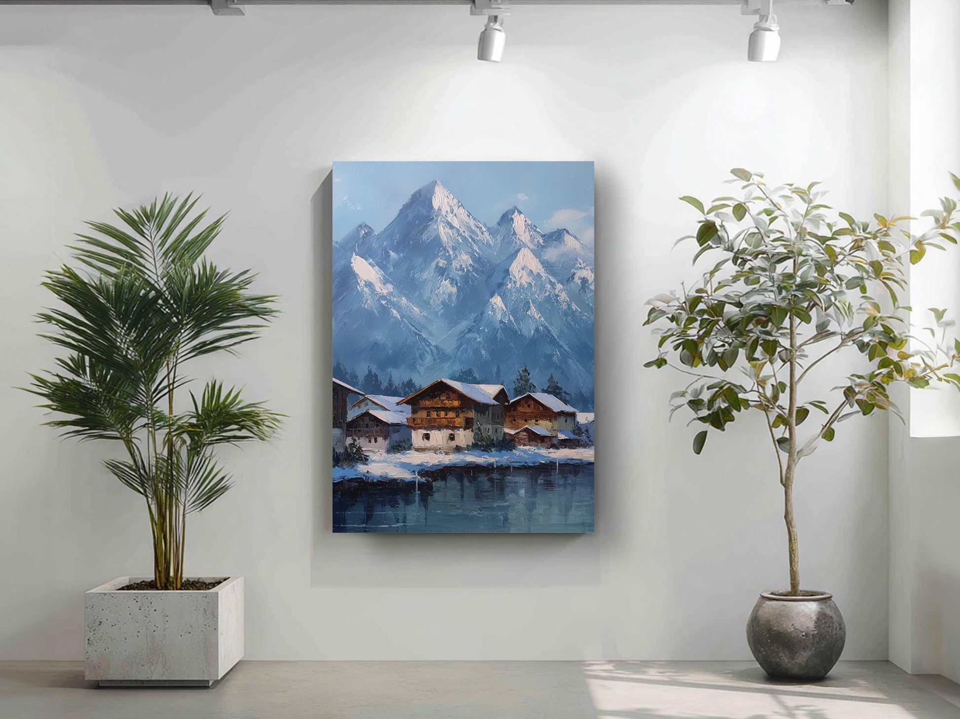 a painting of a snowy mountain village with a lake in the foreground, surrounded by lush greenery. The painting is hung on a white wall, with two potted plants placed on either side of it.