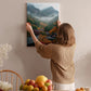 A woman hangs a framed picture of a mountainous landscape on a wall in a cozy room with a dining table, chairs, and various fruits.