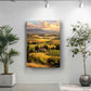a large landscape painting hanging on a wall, with a potted plant to the left and a potted plant to the right.