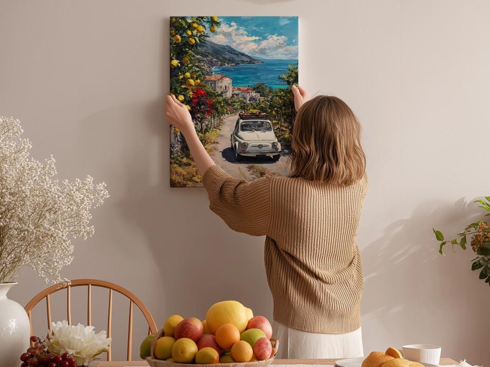 A woman hangs a framed painting of a car on a wall, surrounded by a cozy indoor setting with a dining table, chairs, and various fruits.