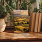 a wooden table with a framed landscape painting depicting a countryside scene, surrounded by potted plants and books.
