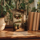 a wooden table with a framed painting of a kitchen scene, surrounded by potted plants and books.