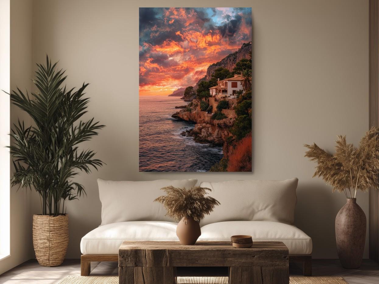 a serene living room with a large painting of a cliffside overlooking the ocean hanging on the wall. The painting captures a breathtaking sunset over the water, with the sky filled with vibrant orange and pink hues. The room is decorated with a white sofa, a wooden coffee table, and potted plants, creating a cozy and inviting atmosphere.