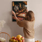 A woman hangs a framed photograph of a chef in a kitchen on a wall.