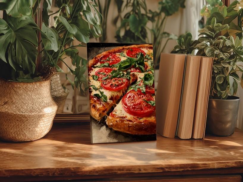 A framed photograph of a pizza with tomato and basil toppings is displayed on a wooden surface, surrounded by potted plants and books.