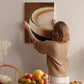 A woman hangs a large picture of a cup of coffee on a wall in a cozy kitchen setting.