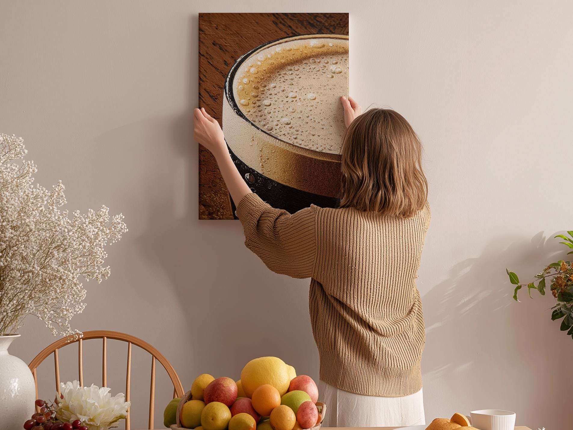 A woman hangs a large picture of a cup of coffee on a wall in a cozy kitchen setting.