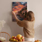 A woman hangs a framed picture of a coastal landscape on a wall, surrounded by a dining table with fruit and flowers.