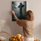 A woman hangs a framed image of a cross on a wall, with a table of fruit and flowers in the foreground.