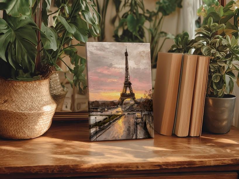 a framed painting of the Eiffel Tower in Paris, surrounded by potted plants and books on a wooden surface.