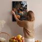 A woman hangs a framed photograph of a market scene on a wall, surrounded by various fruits and flowers in a cozy, homely setting.
