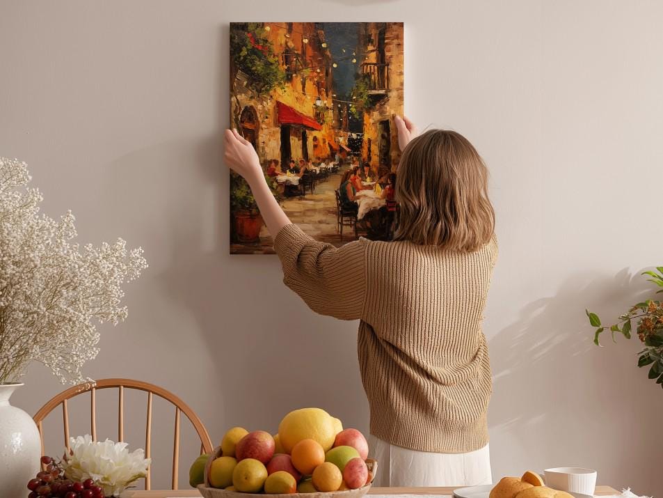 A woman hangs a painting of a city street scene on a wall in a cozy, homely setting.