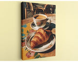 A croissant on a floral plate and a cup of coffee on a wooden table, with a wicker chair visible in the background.