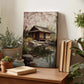 a wooden table with a painting of a Japanese-style house, surrounded by potted plants and books, creating a serene and cozy atmosphere.