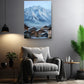 a cozy living room with a comfortable gray armchair, a wooden side table, and a potted plant. Above the armchair, there is a large painting of a snowy mountain village, creating a serene and picturesque atmosphere in the room.