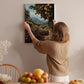 A woman hangs a framed picture of an orange grove on a wall in a cozy room with a dining table, chairs, and various fruits.