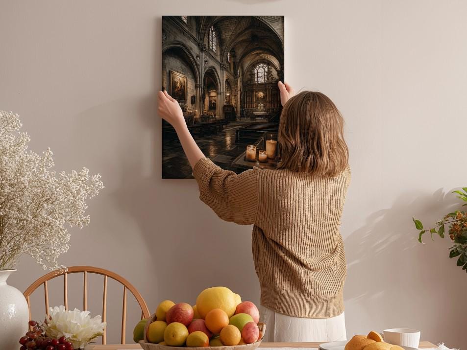 A woman hangs a framed photograph of a church interior on a wall in a room with a dining table, chairs, and various decorative items.