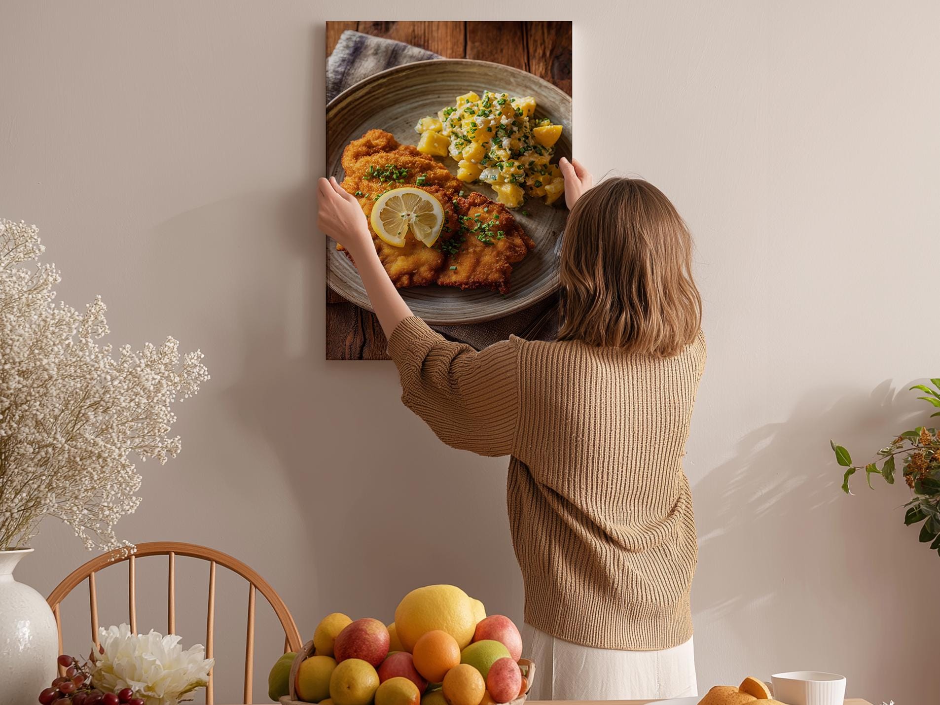 A woman hangs a framed photograph of a plate of food on a wall in a cozy kitchen setting.