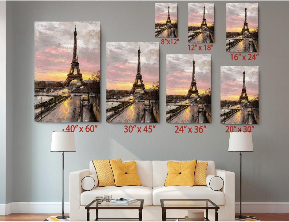 The image is a living room with a white sofa and a coffee table. Above the sofa, there are six framed pictures of the Eiffel Tower, each with a different size and resolution, ranging from 8 x 12 to 24 x 36 inches. The pictures are arranged in a grid-like pattern on the wall, creating a visually appealing display.