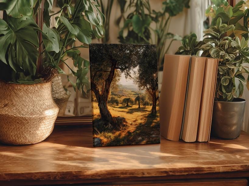 a wooden table with a framed landscape painting depicting a scenic countryside view, surrounded by potted plants and books.