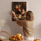 A woman hangs a painting of a fruit arrangement on a wall in a cozy, homely setting.