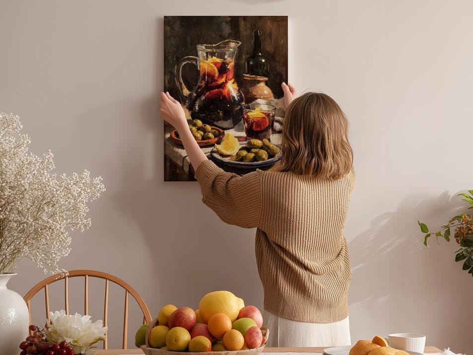 A woman hangs a painting of a fruit arrangement on a wall in a cozy, homely setting.