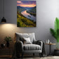 a cozy living room with a comfortable gray armchair, a small side table, and a potted plant. Above the armchair, there is a large framed picture depicting a scenic view of a river with a boat on the water, surrounded by mountains and lush greenery.