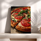 A framed painting of a pizza with tomato and basil toppings is displayed on a white shelf against a white wall.