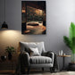 a cozy living room with a comfortable gray armchair, a wooden side table, and a potted plant. Above the armchair, there is a framed picture of a serene garden scene with a wooden bench and a small pond. The room is illuminated by a hanging lamp, creating a warm and inviting atmosphere.