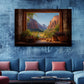 a large painting of a scenic mountain landscape hanging on a blue wall above a blue sofa with pink throw pillows.