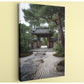 A traditional Japanese temple gate surrounded by a serene garden with a stone path leading up to it.