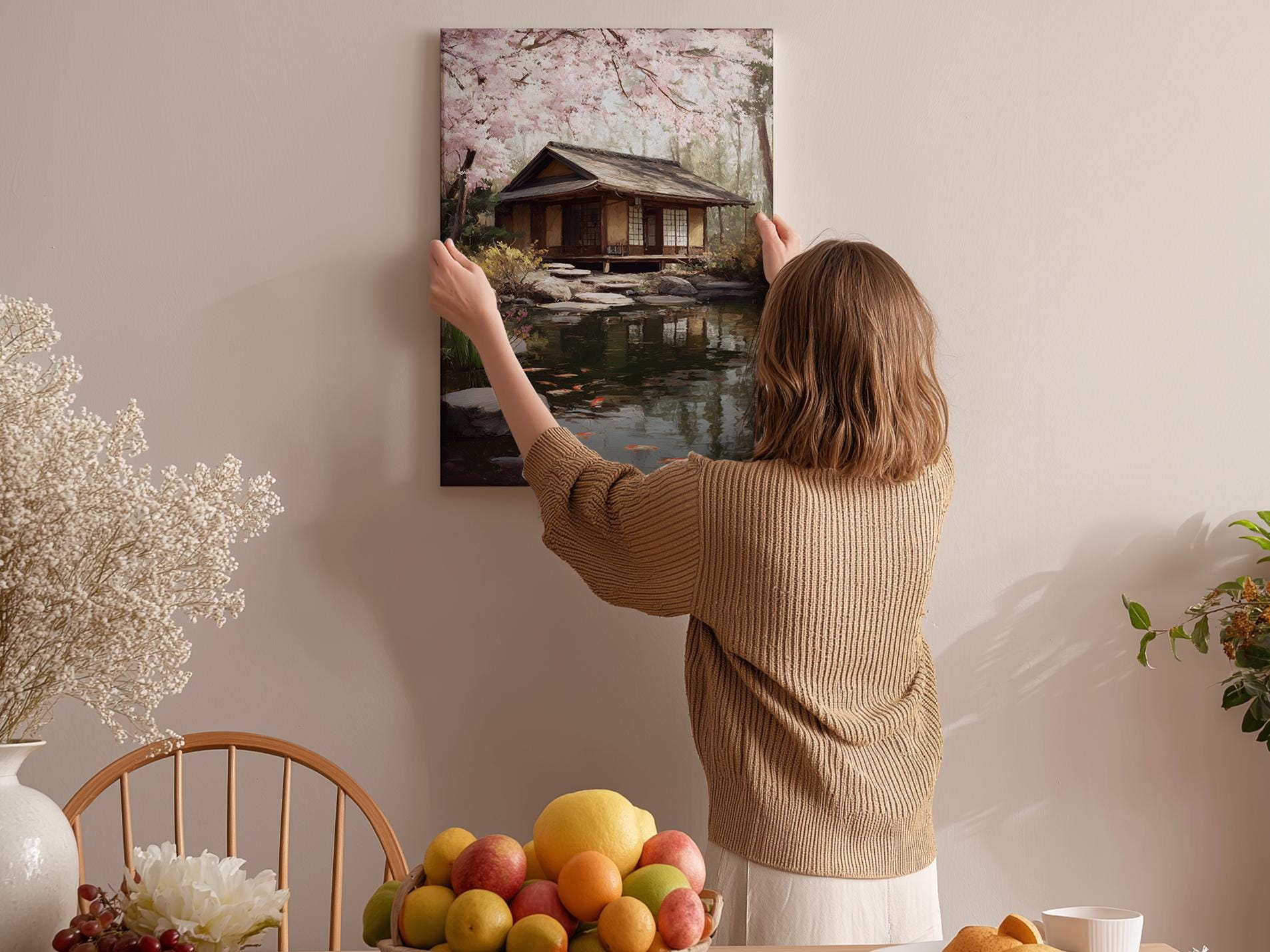 A woman hangs a framed picture of a serene Japanese garden on a wall in a cozy room.
