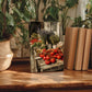a wooden table with a framed photograph of a vegetable market scene, surrounded by potted plants and books.