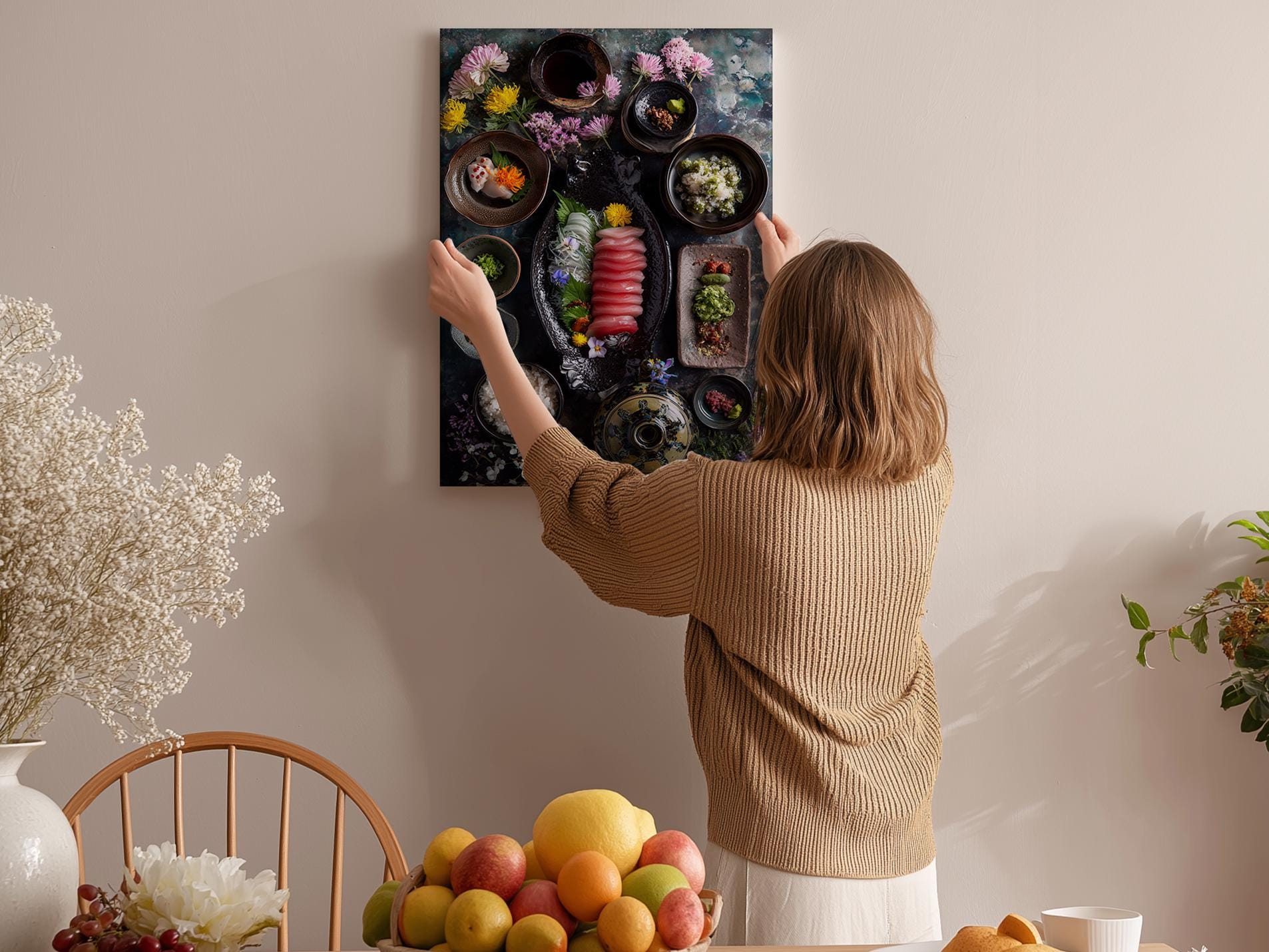 A woman hangs a framed picture of a fruit platter on a wall in a cozy kitchen setting.