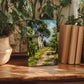 a painting of a house on a path surrounded by trees, displayed on a wooden surface. The painting is accompanied by a stack of books and several potted plants, creating a cozy and artistic atmosphere.