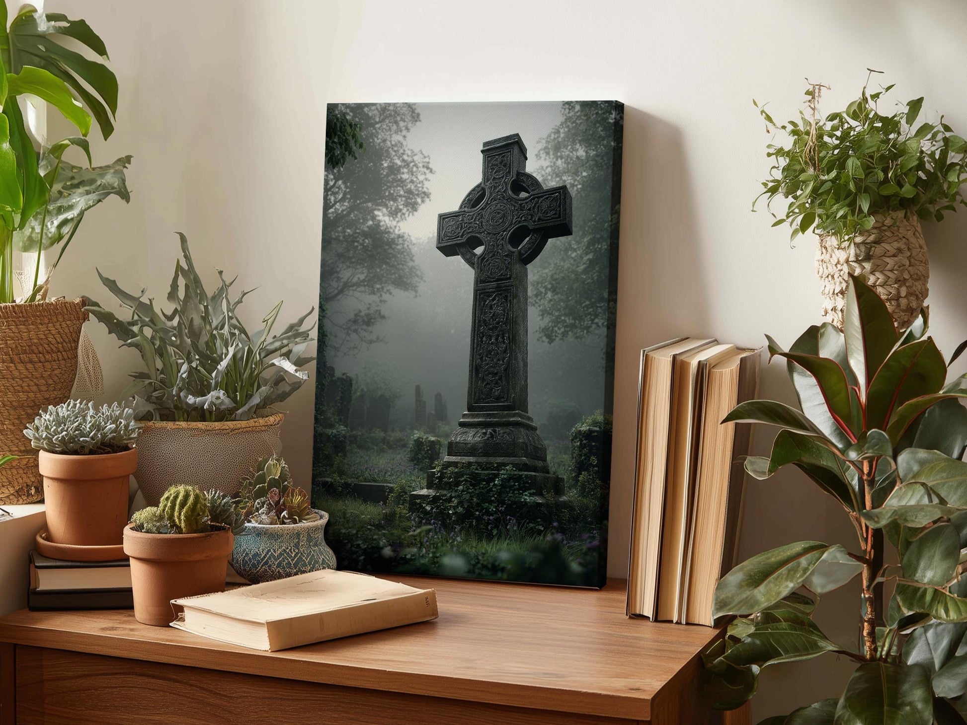 a wooden table with a framed photograph of a cross in a foggy graveyard, surrounded by potted plants and books.