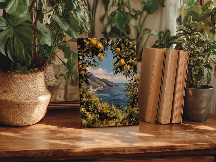 a wooden table with a framed painting of a scenic coastal landscape, surrounded by potted plants and books.