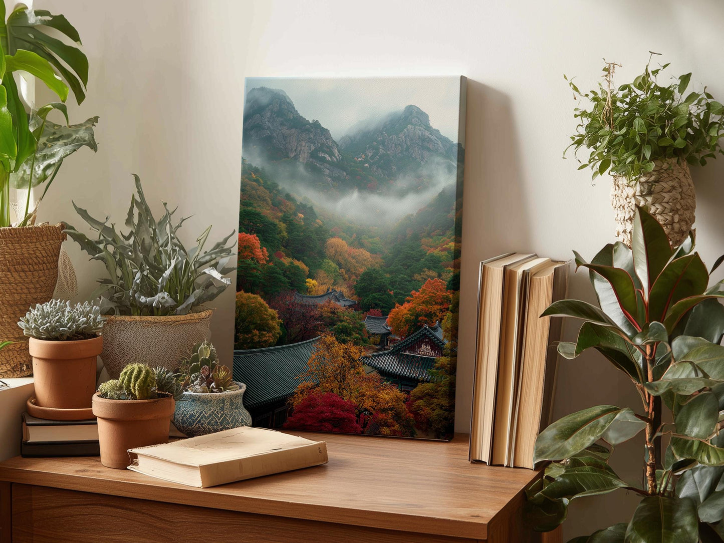 a wooden desk with a framed landscape photograph of a mountainous, forested area with a misty, hazy atmosphere. The desk also has several potted plants, books, and other decorative items.